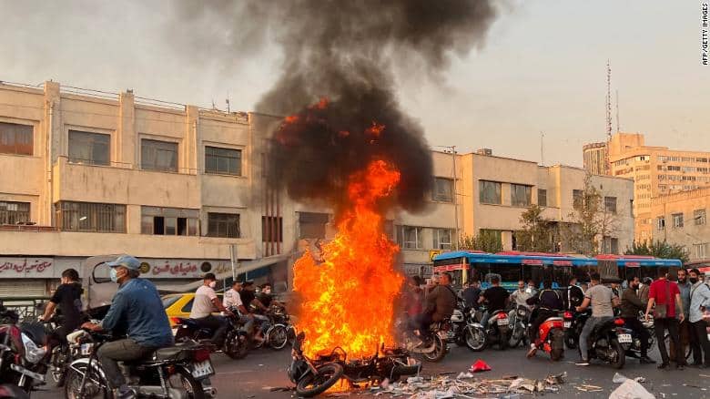 A picture obtained by AFP outside Iran, shows people gathering next to a burning motorcycle in the capital Tehran on October 8, 2022.