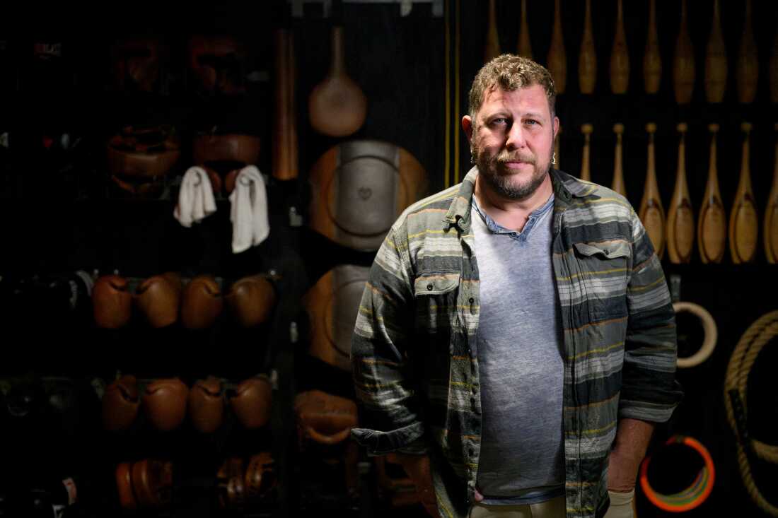 This photo is a portrait of Josh Parise. The photo shows him from the waist up, and he's wearing a gray shirt with an unbuttoned horizontal-striped shirt on top of it.