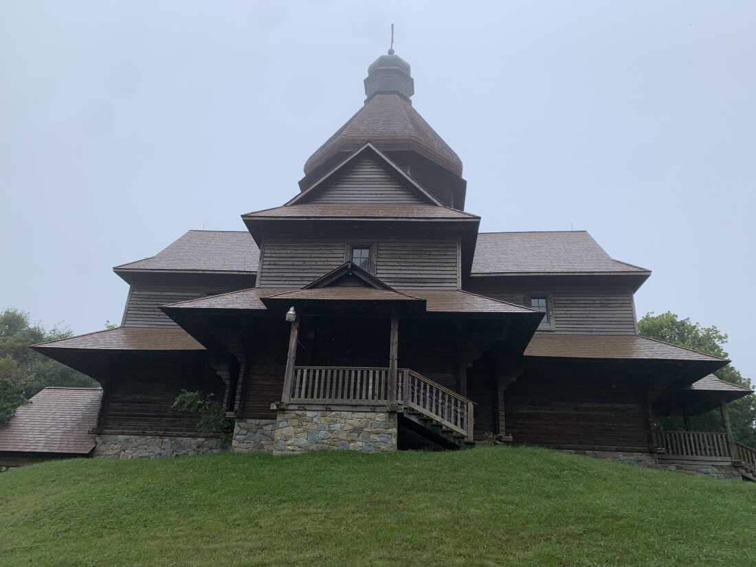 Holy Trinity Particular Ukrainian Catholic Church is a wooden building with a stone foundation and sits atop green grass.