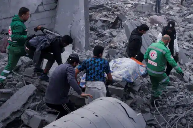 رجال الدفاع المدني ومدنيون يحملون جثمان فلسطيني في موقع غارة إسرائيلية على منازل سكنية، في مدينة غزة، 4 يناير/كانون الثاني 2025