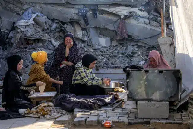 نساء يعدن الطعام للإفطار في اليوم الأول من شهر رمضان المبارك، بينما يجلسن بجوار أنقاض مبنى منهار في ملجأ في جباليا شمال قطاع غزة في الأول من مارس/آذار 2025