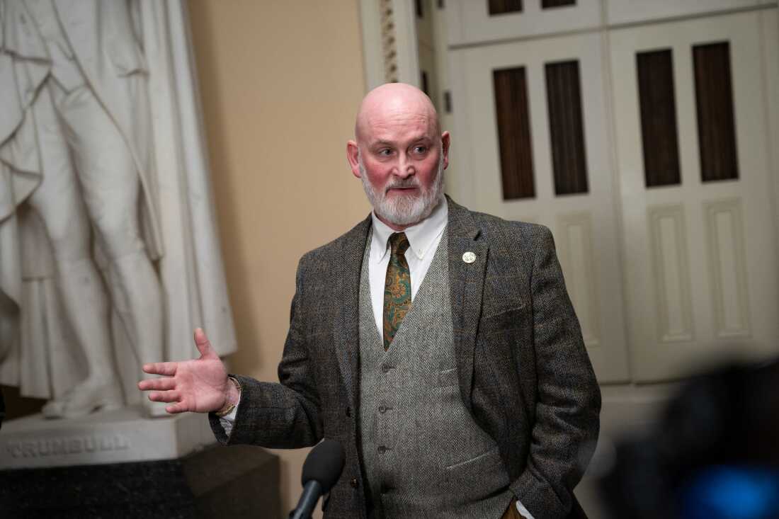 Republican Rep. Derrick Van Orden of Wisconsin has a gray beard and is wearing a dark plaid blazer over a gray vest. He standing next to a marble statue on Capitol Hill. 