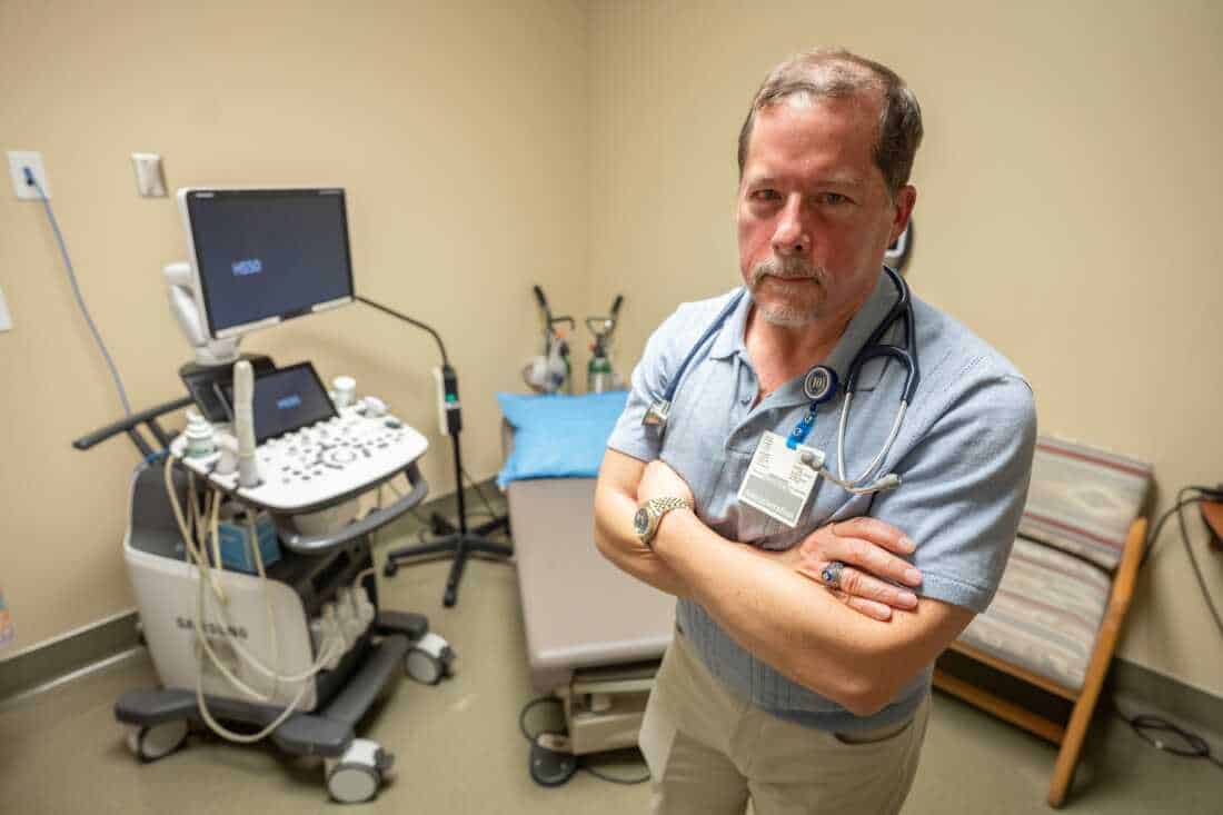 Dr. Carmelo Hernandez is shown in a portrait in an exam room with an ultrasound machine.