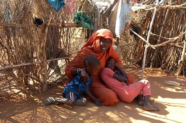 أم سودانية نازحة مع أطفالها، تجلس على الأرض في مخيم زمزم الذي يعاني من المجاعة، شمال دارفور، في 21 يناير/كانون الثاني 2025.