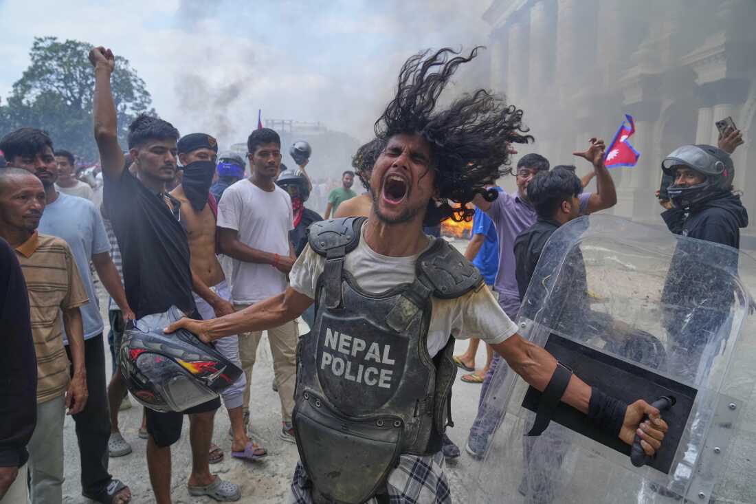 A protester wearing a flak jacket and carrying a shield snatched from a policeman shouts slogans at the Singha Durbar, the seat of Nepal's government's various ministries and offices, during a protest against a social media ban and corruption in Kathmandu, Nepal, Tuesday.