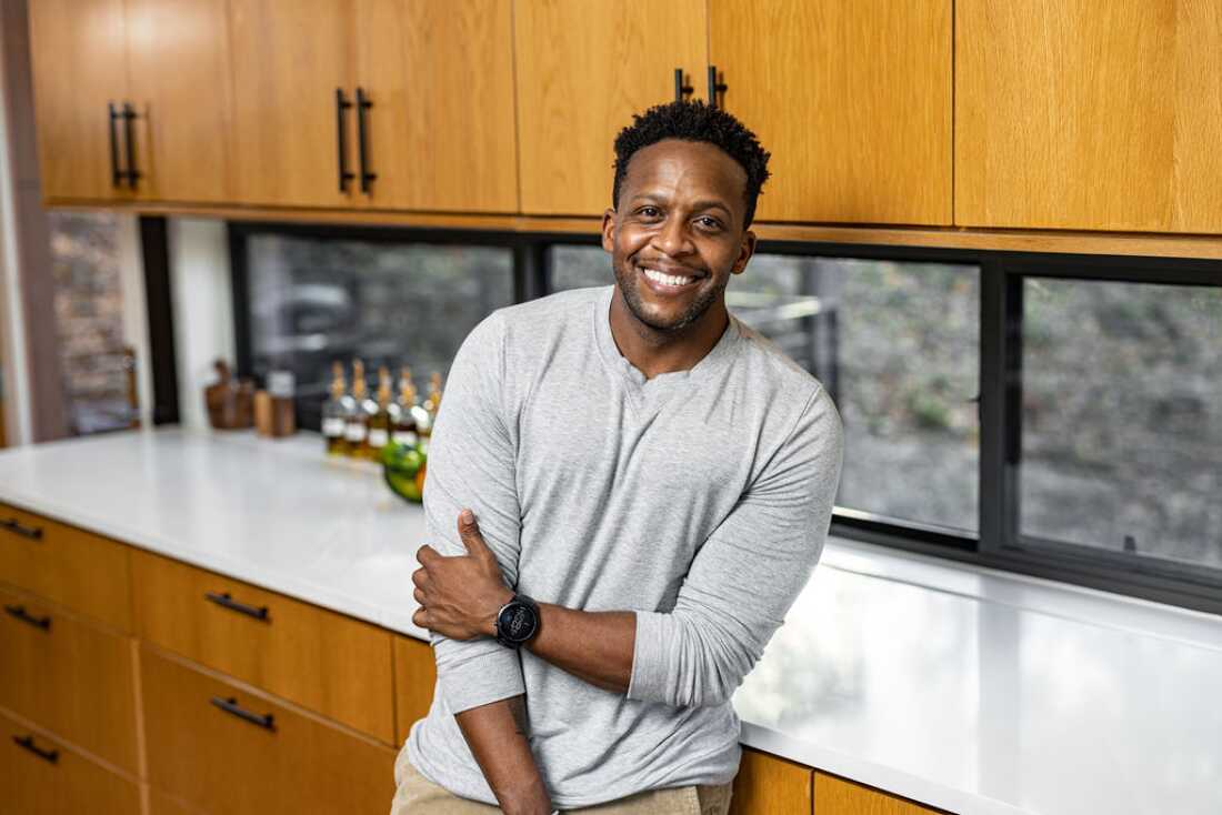 A portrait of food influencer Kevin Curry leaning against a kitchen counter and smiling at the camera. 