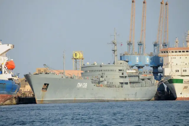 صورة أرشيفية لسفينة مخصصة للإصلاح تابعة للبحرية الروسية من فئة آمور، PM-138، راسية في ميناء مدينة بورتسودان السودانية. السفينة كبيرة تميل للون الرمادي حولها عدد من السفن والقوارب. الصورة التقطت نهاراً.