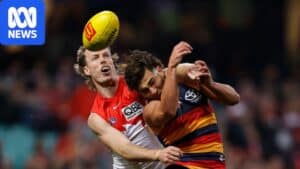Sydney Swans and Adelaide Crows players contest the ball at the SCG in wet conditions.